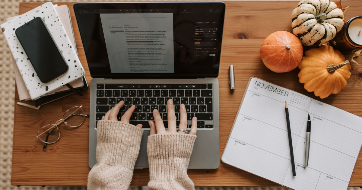 A person working at a laptop with a planner on the desk